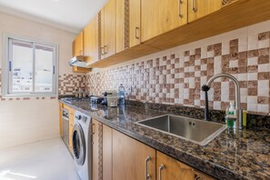 Cozinha com armários de madeira, pia de aço inoxidável, máquina de lavar e painel de azulejos.