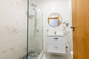 A bathroom with a glass-enclosed shower, a round mirror, a white sink, and a wooden door. - Splendid bright 2BR apartment in central Tangier (Tangier)