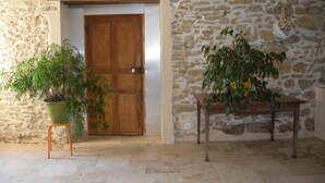 Une pièce avec un mur en pierre, une porte en bois, une plante en pot posée sur un tabouret et une table en bois.