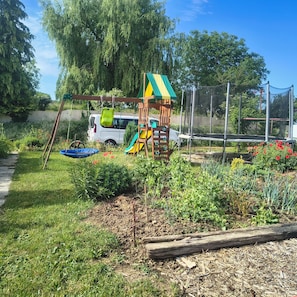 Ein Spielplatz mit Rutsche und Klettergerüst, umgeben von viel Grün und einem geparkten Fahrzeug.
