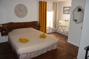 Une chambre à coucher avec un lit, une petite table, une chaise, un miroir et une fenêtre avec des rideaux.