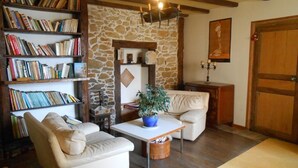 Un salon chaleureux avec un mur en pierre, une bibliothèque, un canapé, une table basse et une porte en bois.