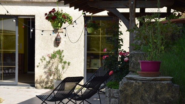 Une terrasse avec deux chaises longues noires, une jardinière suspendue et une plante en pot posée sur une étagère en pierre.