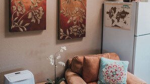 Un salon comprenant un canapé, une plante en pot, un réfrigérateur et deux grands tableaux représentant des motifs floraux accrochés au mur.