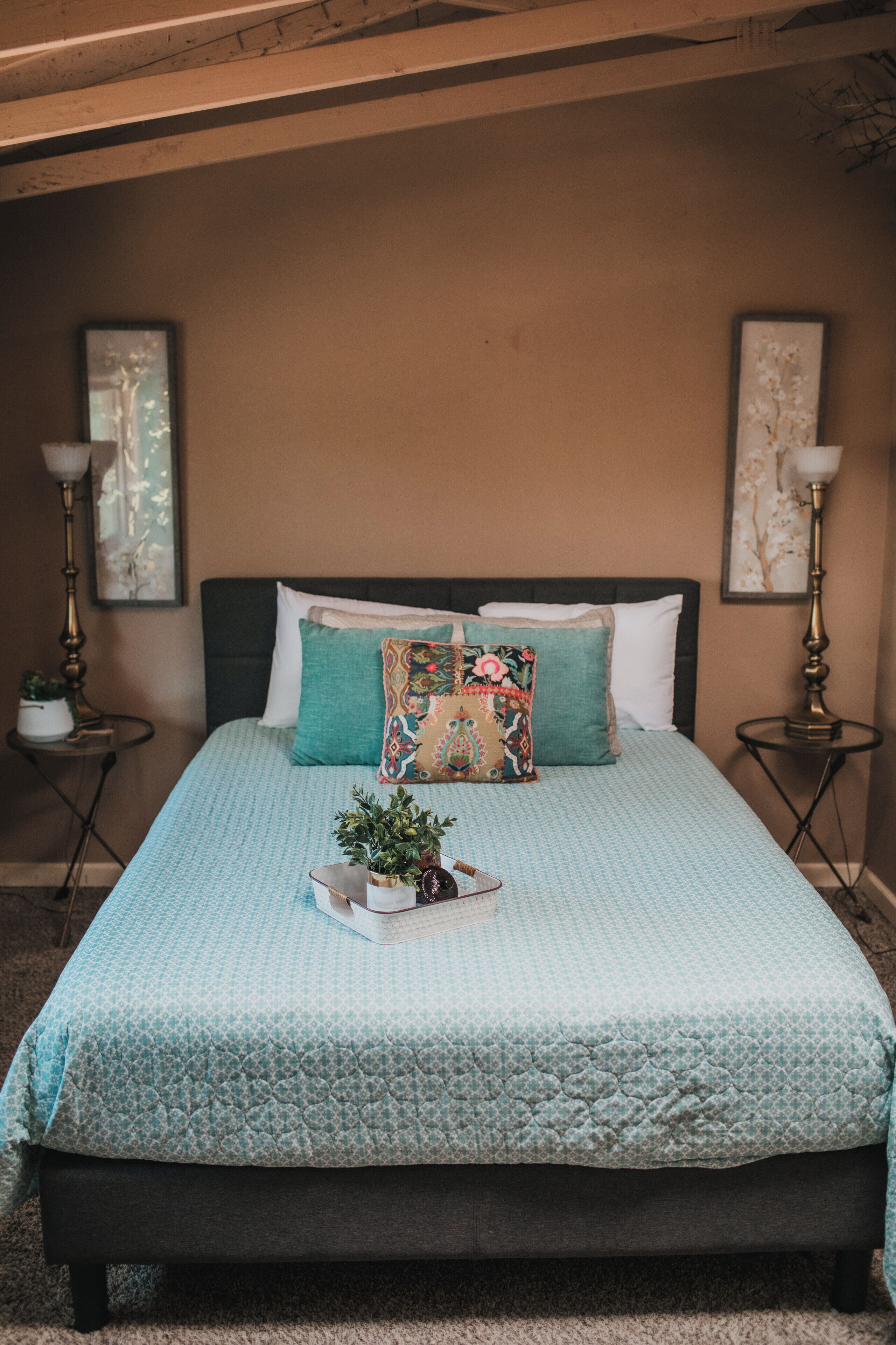 A bedroom with a bed, pillows, a bedside table, a lamp, and a wall-mounted artwork.