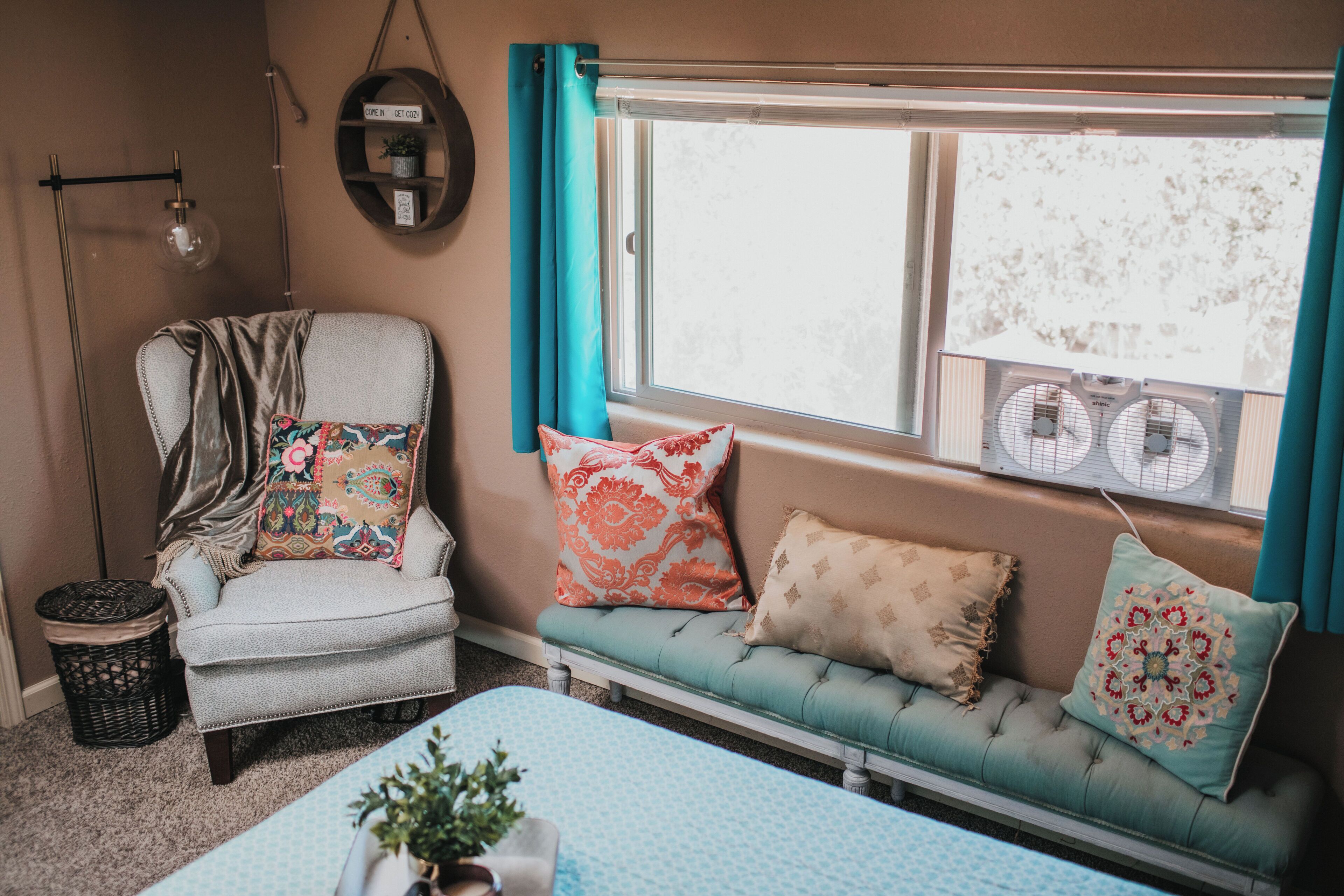 A cozy room with a vintage armchair, a cushioned bench, and a window with curtains.