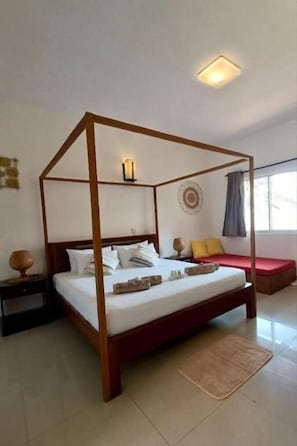 Ein Himmelbett mit hölzernem Gestell, ein Nachttisch, eine Wandlampe und ein Fenster mit Vorhängen.