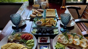 A table set with various breakfast items including eggs, toast, and pastries, with a menu and a view of the street outside. - La Fontaine de Tara Boutique Hotel (Siem Reap)