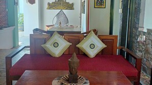 A room with a wooden table, two chairs, a red sofa, and a decorative Buddha statue. - La Fontaine de Tara Boutique Hotel (Siem Reap)