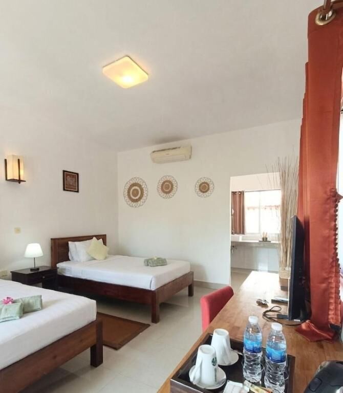 Quarto de hotel com duas camas, uma escrivaninha com computador, abajur e televisão.