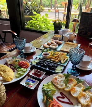 Ein reichhaltiges Frühstücksbuffet auf einem Holztisch mit Blick auf grüne Natur.