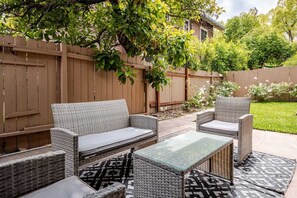 Eine Terrasse mit Korbmöbeln, einem Glastisch und einem gemusterten Teppich.