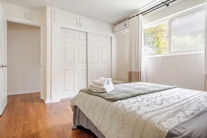 Ein Schlafzimmer mit Bett, Kleiderschrank und einem Vorhangfenster.