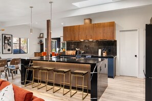 A modern kitchen with a central island, bar stools, and a dining area with a sofa. - Midcentury Modern Oasis: Atomic Ranch Reimagined (Davis)
