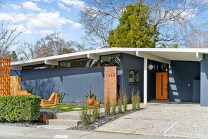 A modern house with a garage, a number '1535' on the garage door, and a small garden with plants and a chair. - Midcentury Modern Oasis: Atomic Ranch Reimagined (Davis)