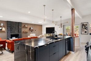 A modern kitchen with a central island, built-in appliances, and a dining area with a red sofa. - Midcentury Modern Oasis: Atomic Ranch Reimagined (Davis)