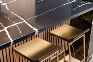 A black marble countertop with white veins, two gold-colored barstools with wooden slats, and a wooden panel wall. - Midcentury Modern Oasis: Atomic Ranch Reimagined (Davis)