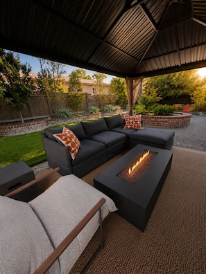 An outdoor patio with a sectional sofa, a fire pit, and a covered area.