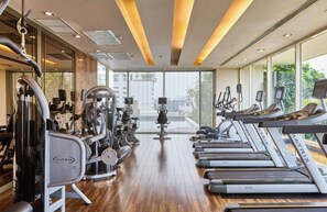 Ein Fitnessstudio mit Cardiogeräten, Krafttrainingsmaschinen und Blick auf Gebäude durch große Fenster.