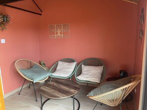 Ein Zimmer mit drei Korbstühlen, einem kleinen Holztisch und einer an der Wand hängenden Holzskulptur.