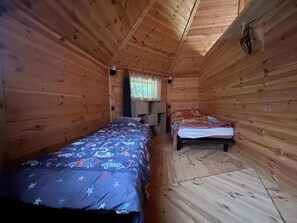 Eine Holzhütte mit zwei Betten, Holzwänden, einem Fenster mit Vorhängen und einer Deckenleuchte.