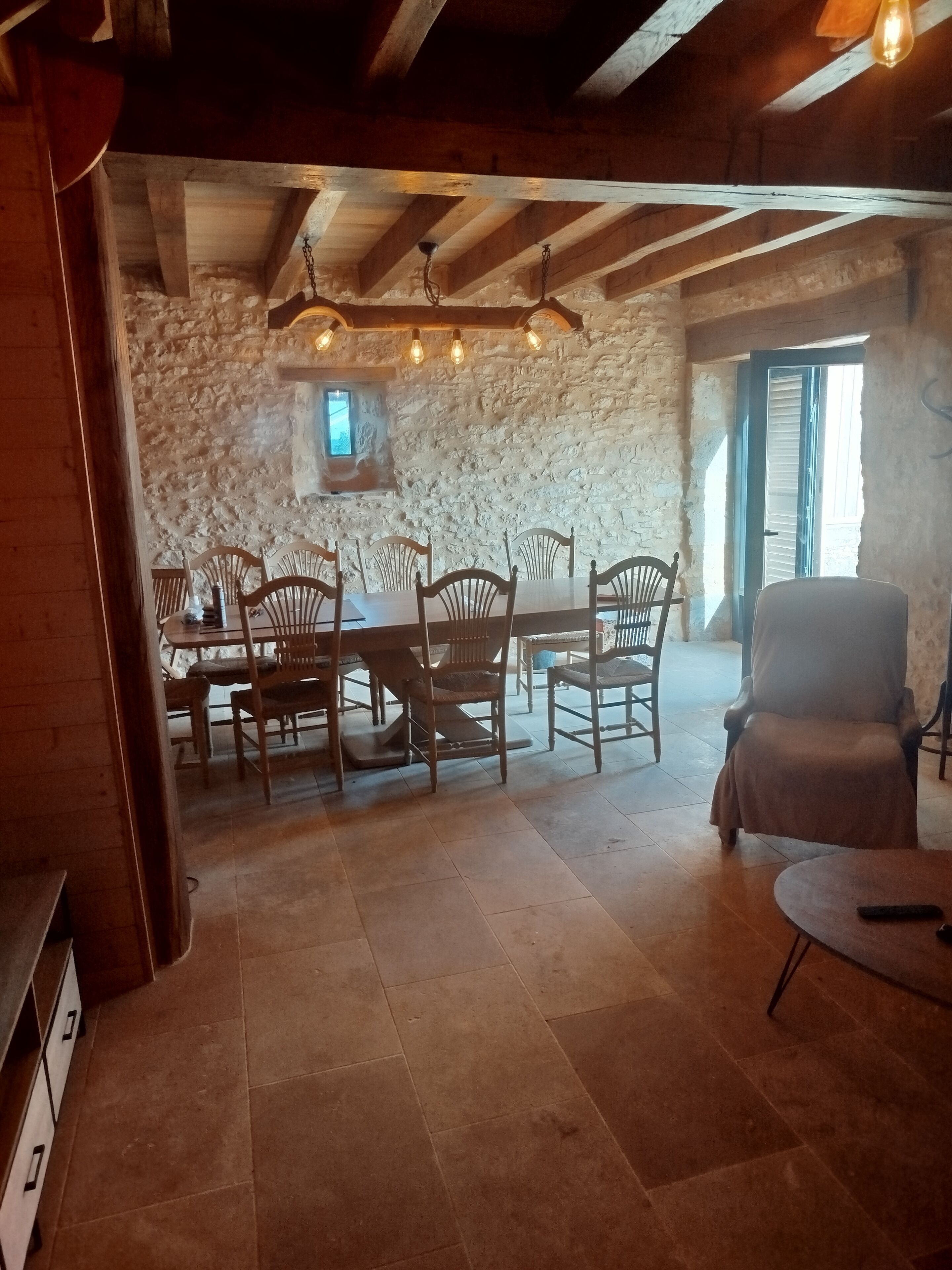 Un espace repas agrémenté d’un mur en pierre, de poutres en bois au plafond et d’une table avec des chaises.