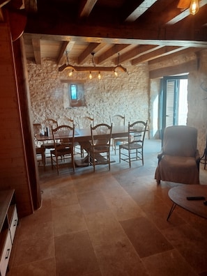 A dining area with a stone wall, wooden ceiling beams, and a table with chairs. - House in the heart of the Périgord Noir (Coux et Bigaroque-Mouzens)
