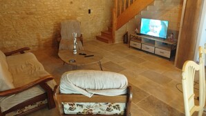 Un salon chaleureux avec un mur en pierre, des meubles en bois, un téléviseur et un escalier.