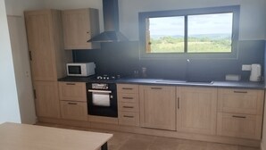 Une cuisine moderne avec des meubles de couleur bois clair, une hotte noire, un four à micro-ondes et une fenêtre donnant sur un paysage verdoyant.
