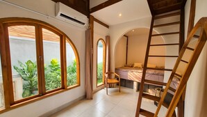 Una habitación con cama, una silla, una escalera y grandes ventanales con vistas a la vegetación.