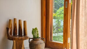 Una habitación con una escultura de madera, una maceta con una planta y vistas a la vegetación a través de una puerta de cristal.