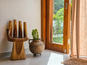 A room with a wooden sculpture, a pot with a plant, and a view of greenery through a glass door. - 3-bedroom family house with pool, garden and toys (Kuta Selatan)