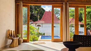 Una habitación con un gran ventanal corredera, piscina y vista a un edificio de techo rojo.