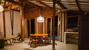 Un comedor con mesa y sillas de madera, una lámpara colgante y vista a una piscina a través de puertas de vidrio.