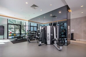 A modern gym with exercise equipment, large windows, and a view of trees. - Romantic 2BR CBD APT W/Pool, Sauna, and Gym (Melbourne)