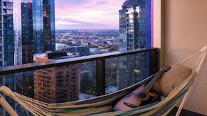 Een hangmat met een gitaar en kussen op een balkon met uitzicht over de stad.