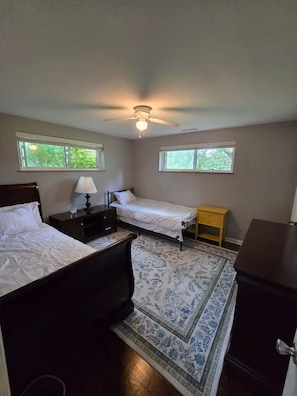 A bedroom with two beds, a ceiling fan, a nightstand, a lamp, a small table, and a patterned rug.