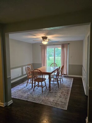 Une salle à manger avec une table et des chaises en bois, un tapis à motifs et un ventilateur de plafond.
