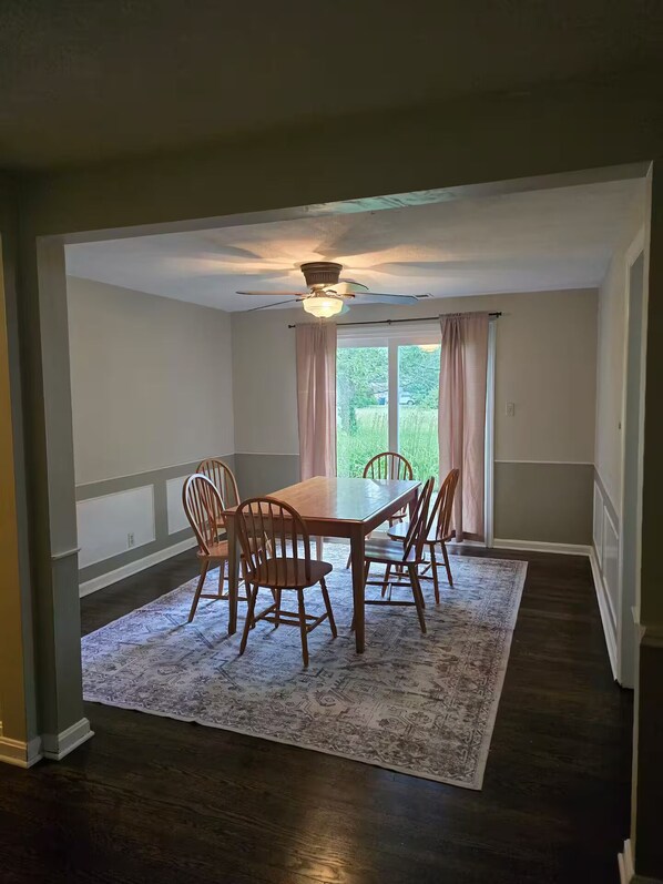 A dining room with a wooden table and chairs, a patterned rug, and a ceiling fan.