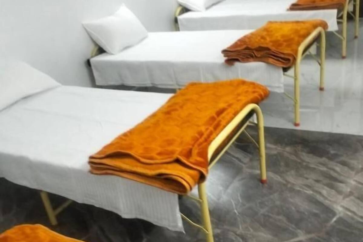 Camas individuales con sábanas blancas y colchas naranjas, dispuestas en línea a lo largo de una pared con suelo de mármol.