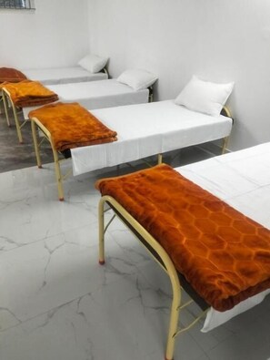 Ein Zimmer mit vier Betten nebeneinander, jedes mit einer weißen Matratze und einer braunen Decke.