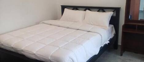 A bed with a white bedspread and pillows, a wooden headboard, and a mirror on the wall.