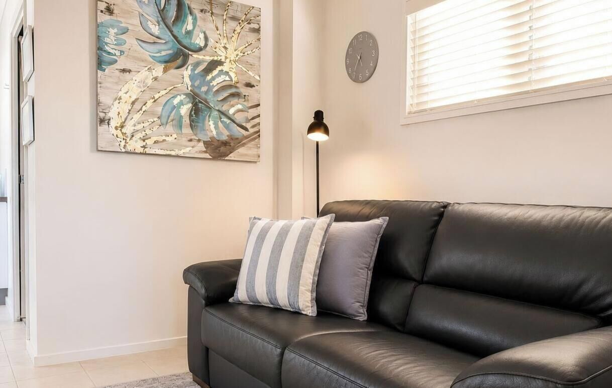 A black leather sofa with striped pillows, a wall clock, and a floor lamp in a room with a large leaf-patterned artwork.