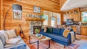 L'interno accogliente di una baita con camino in pietra, pareti in legno, un divano blu, un'area pranzo e una cucina con pensili in legno.