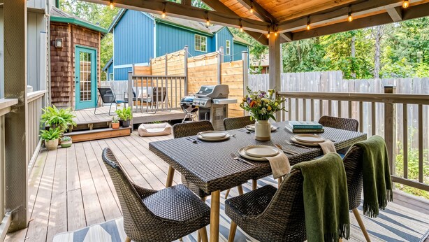 Una veranda riparata con mobili da esterno, un barbecue e vista su una casa blu.