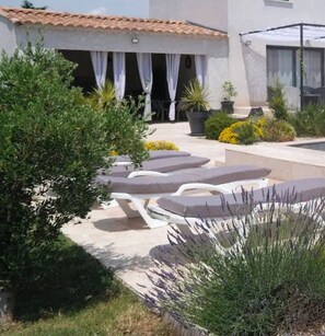 Un patio con sillones de descanso, una zona de estar cubierta y plantas en macetas.