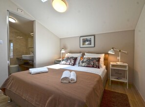 A hotel room with a bed, two bedside lamps, a nightstand, a framed picture on the wall, and a bathroom visible through an open door. - Tranquil Getaway With Shared Pool in Bale - One Bedroom Apartment (Bale)