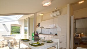 Una cocina moderna con armarios blancos, un comedor con una mesa dispuesta para dos personas, y vistas al exterior a través de un ventanal.