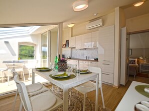 A modern kitchen with white cabinets, a dining area with a table set for two, and a view of the outdoors through a glass door. - Tranquil Getaway With Shared Pool in Bale - One Bedroom Apartment (Bale)