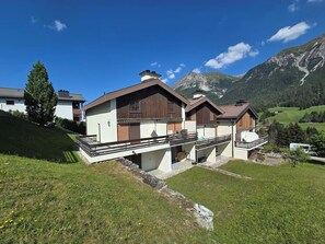 Een moderne chalet met een houten gevel, een balkon en uitzicht op bergen.